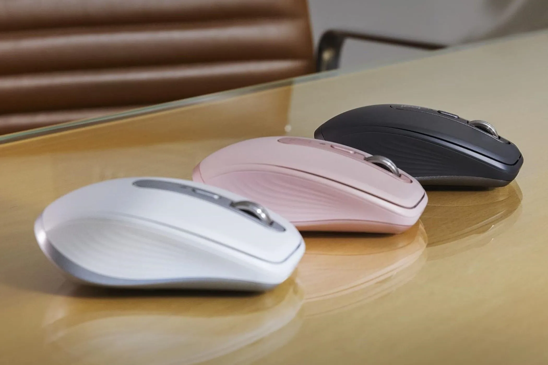 Ba phiên bản chuột Logitech MX Anywhere 3S màu đen, trắng và hồng trên mặt bàn kính, thể hiện khả năng hoạt động trên nhiều bề mặt.