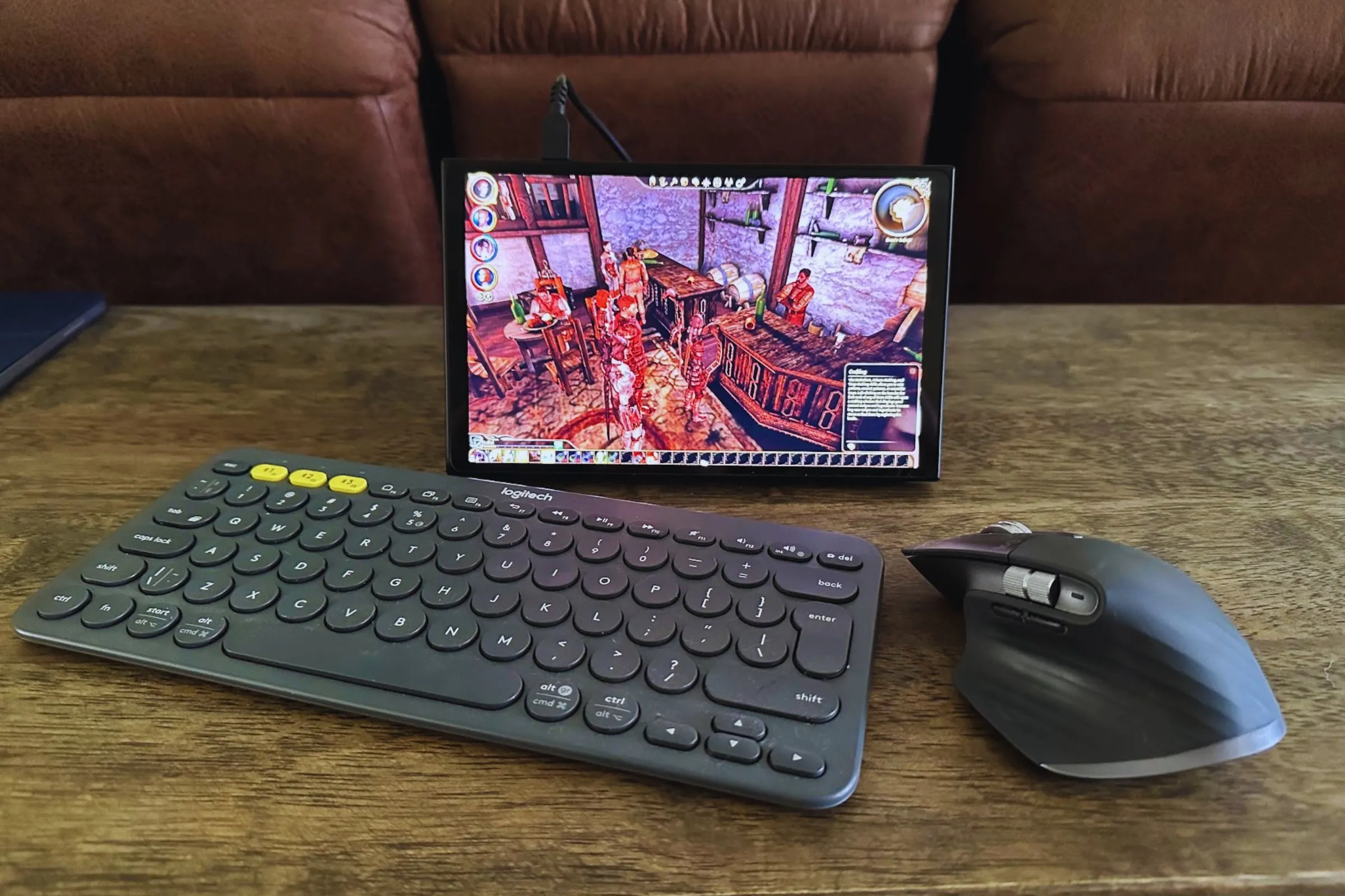Bàn phím Logitech K380, chuột MX Master 3S và thiết bị chơi game cầm tay Lenovo Legion Go trên bàn gỗ.
