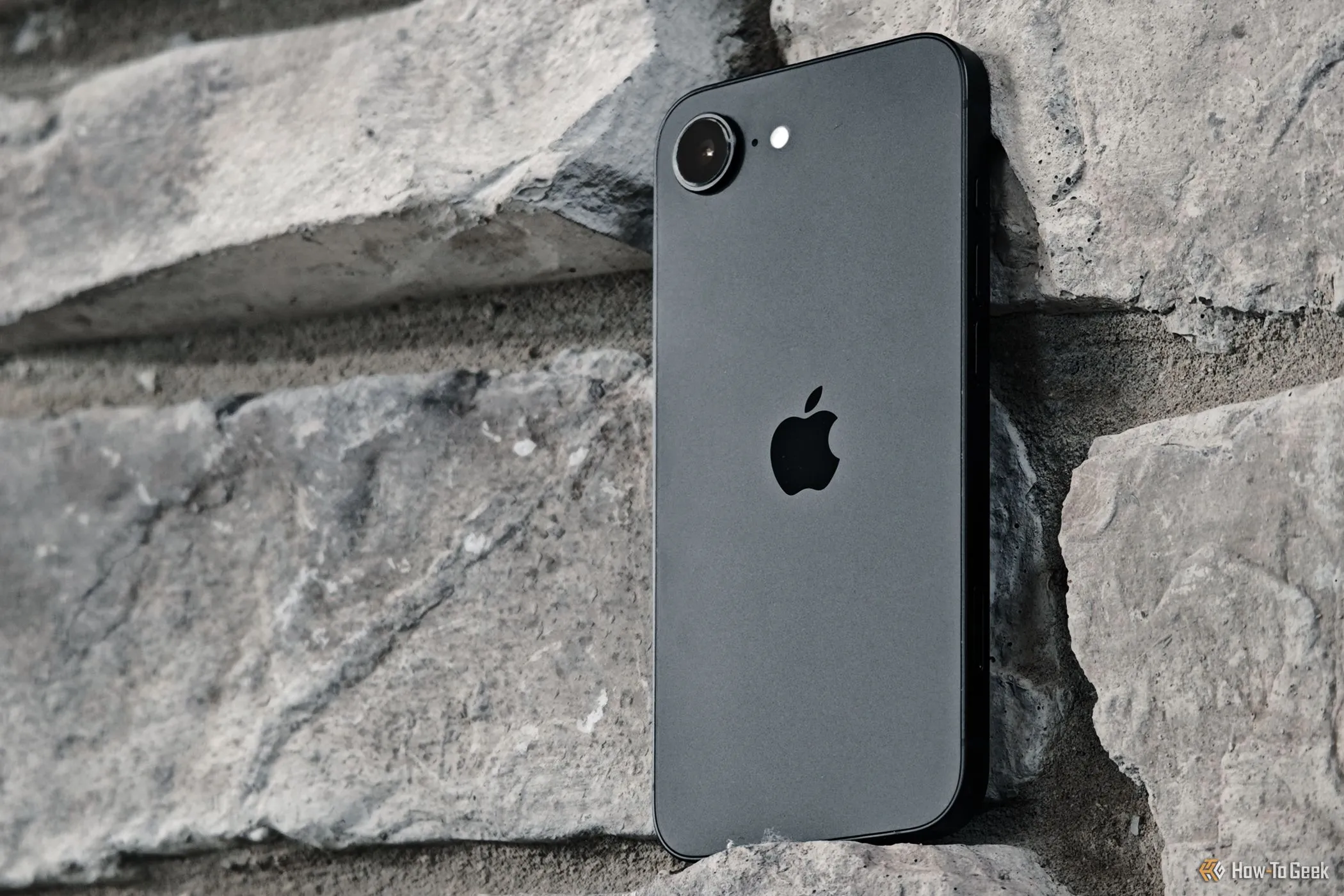 Chiếc iPhone 16e được đặt dựa vào tường gạch, minh họa hạn chế về camera góc siêu rộng