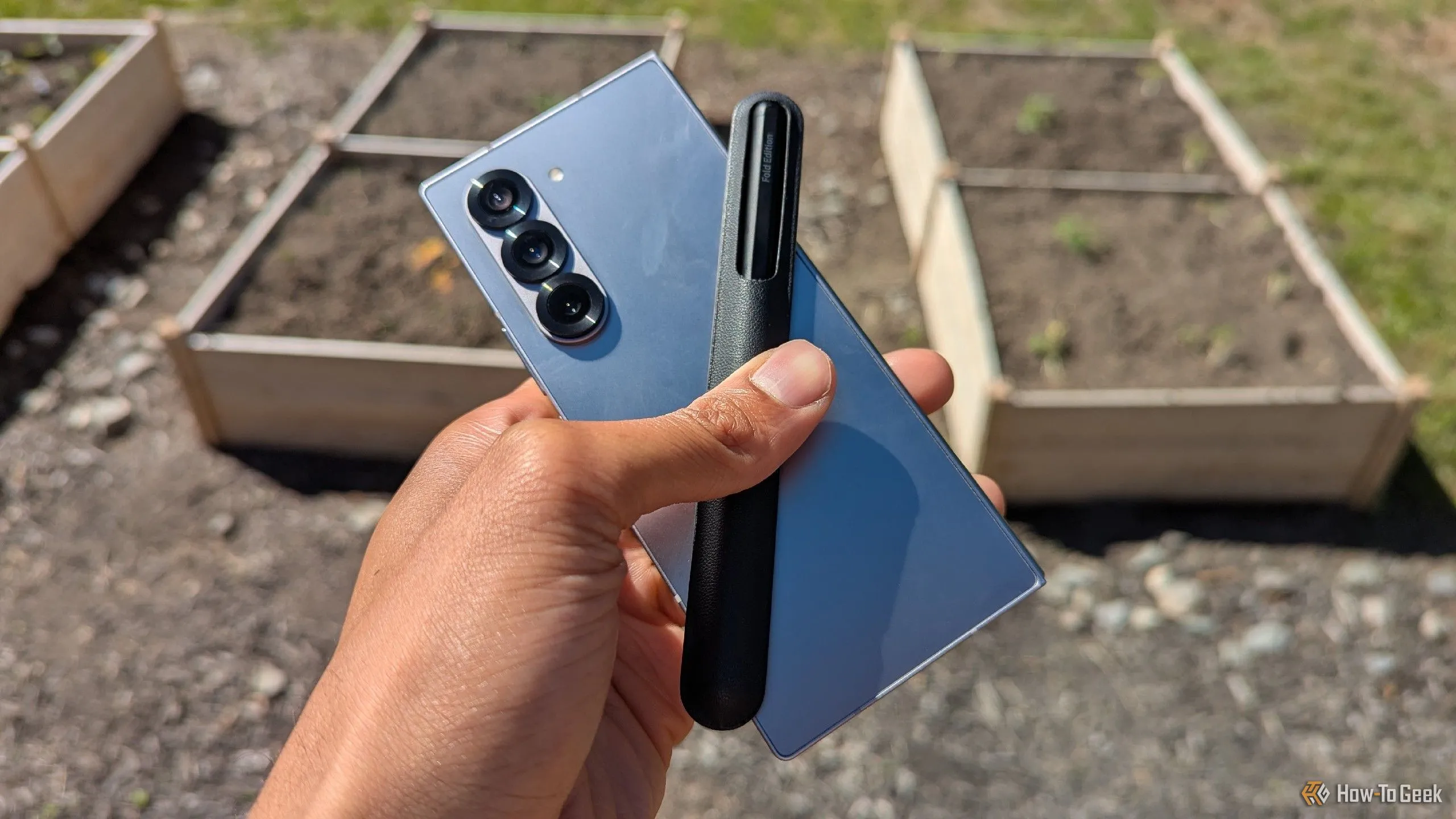 Điện thoại Samsung Galaxy Z Fold 6 mở ra, đi kèm bút S Pen, đặt trước khu vườn xanh tươi, thể hiện độ bền và tính linh hoạt của điện thoại gập.