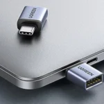 Hai bộ chuyển đổi UGREEN USB-C sang USB-A màu xám bạc, một cái đặt trên máy tính xách tay và một cái đang cắm vào cổng USB-C.