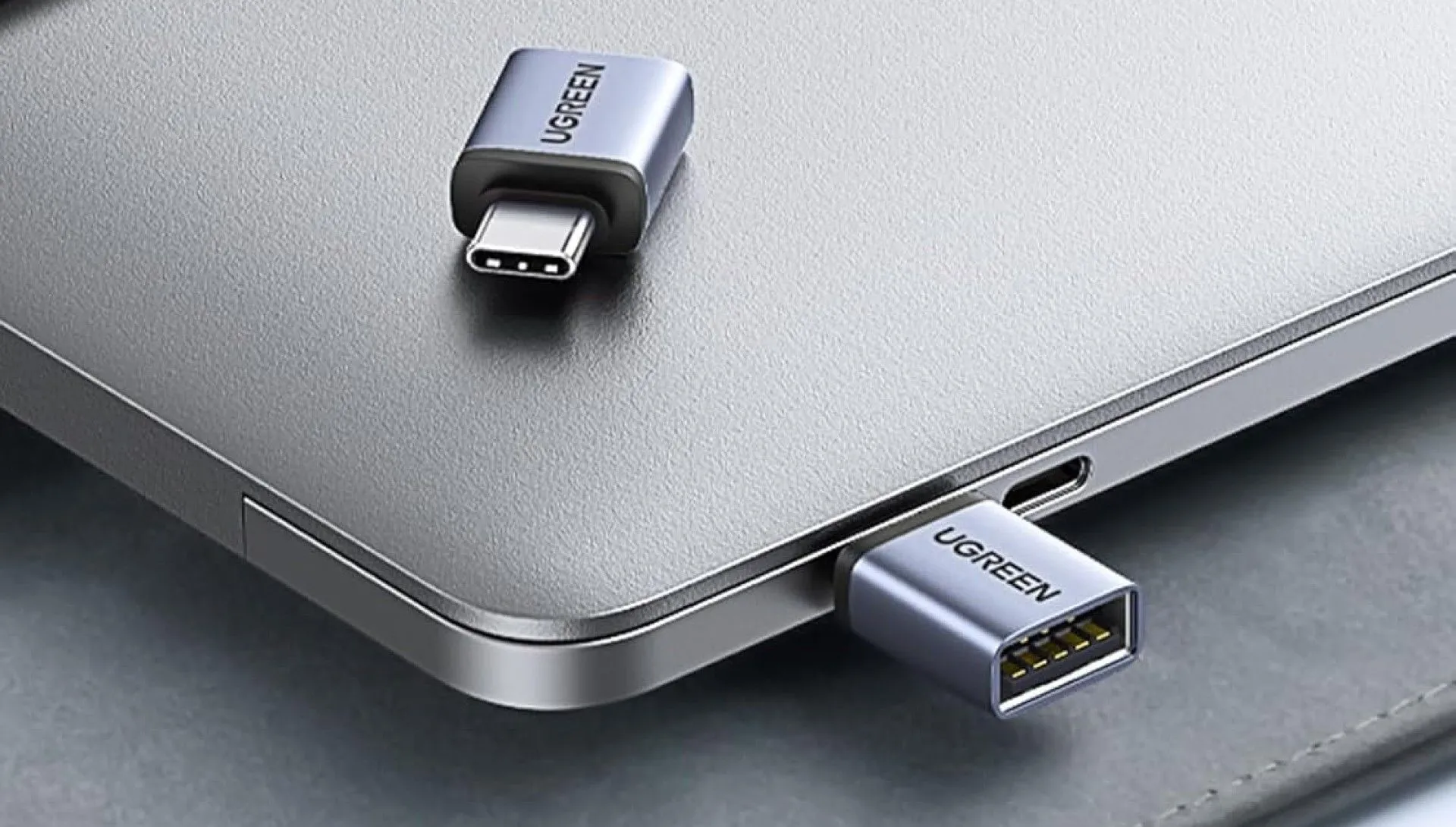 Hai bộ chuyển đổi UGREEN USB-C sang USB-A màu xám bạc, một cái đặt trên máy tính xách tay và một cái đang cắm vào cổng USB-C.