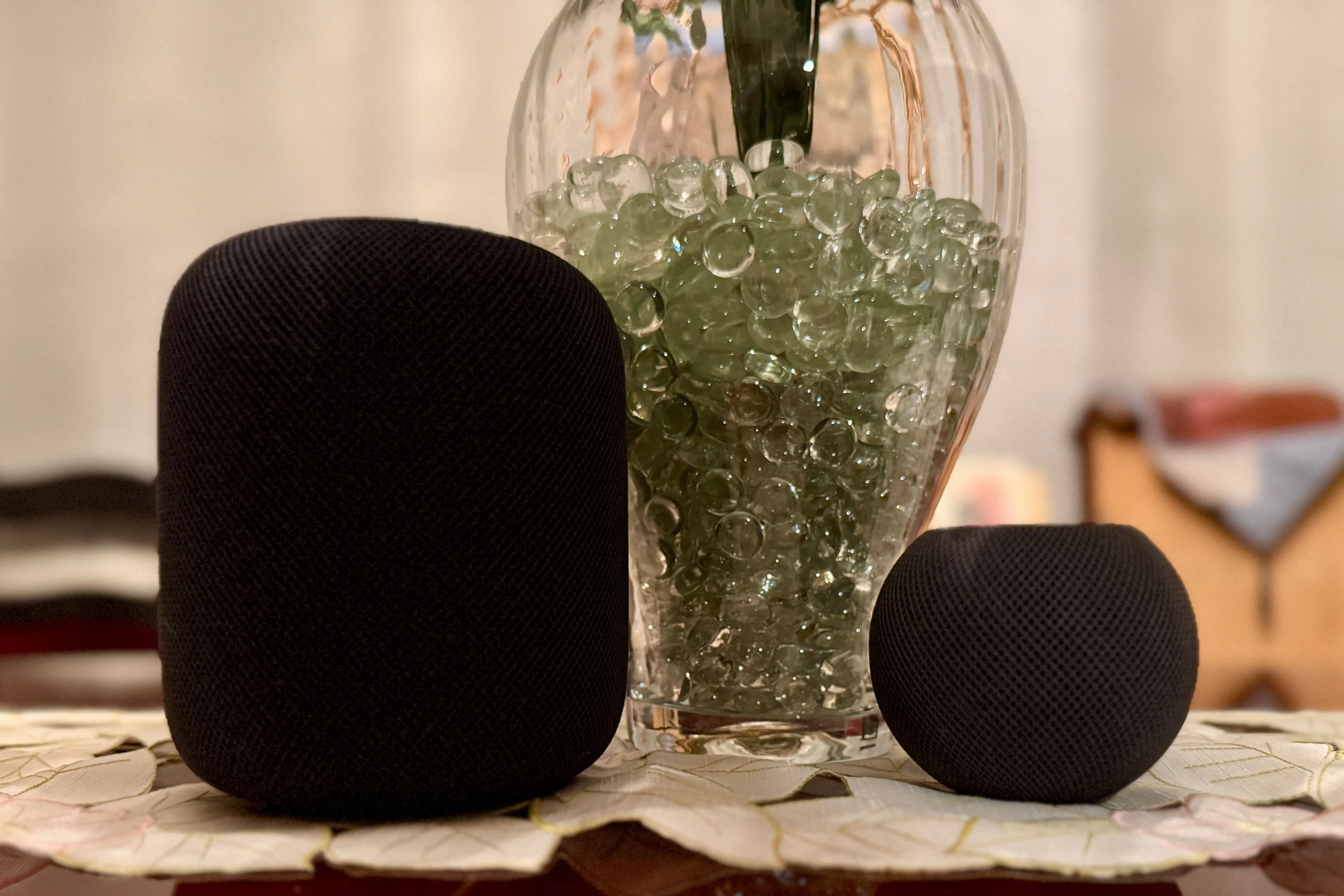 Hai chiếc HomePod màu đen đặt cạnh một chiếc bình chứa hạt trang trí.