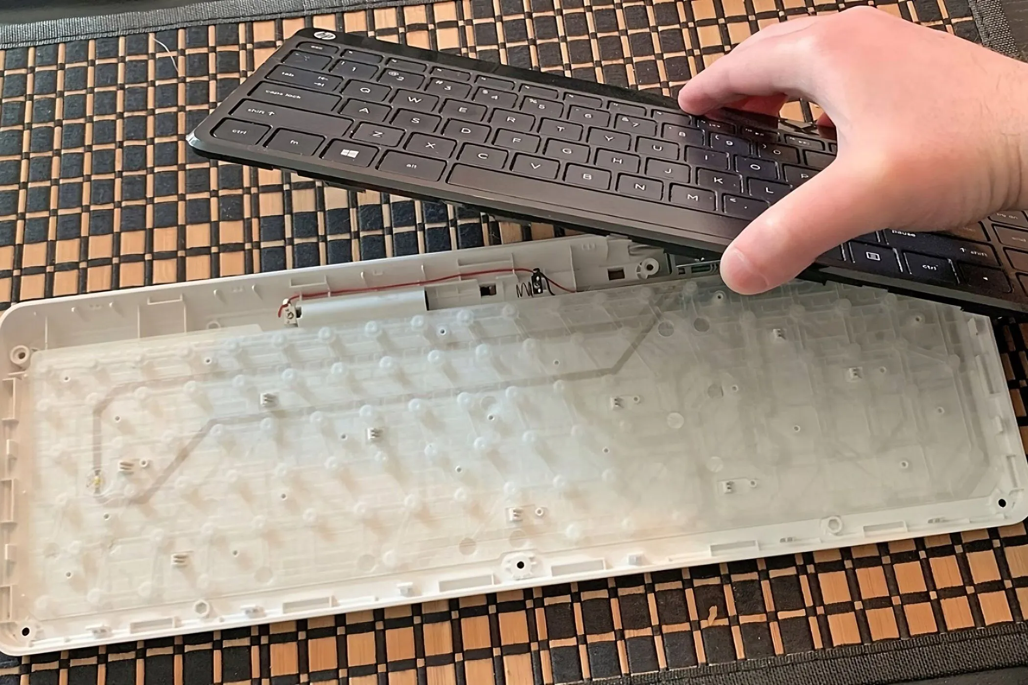 Một bàn phím màng được tách làm hai phần, với một bàn tay giữ các keycap trên lớp màng.