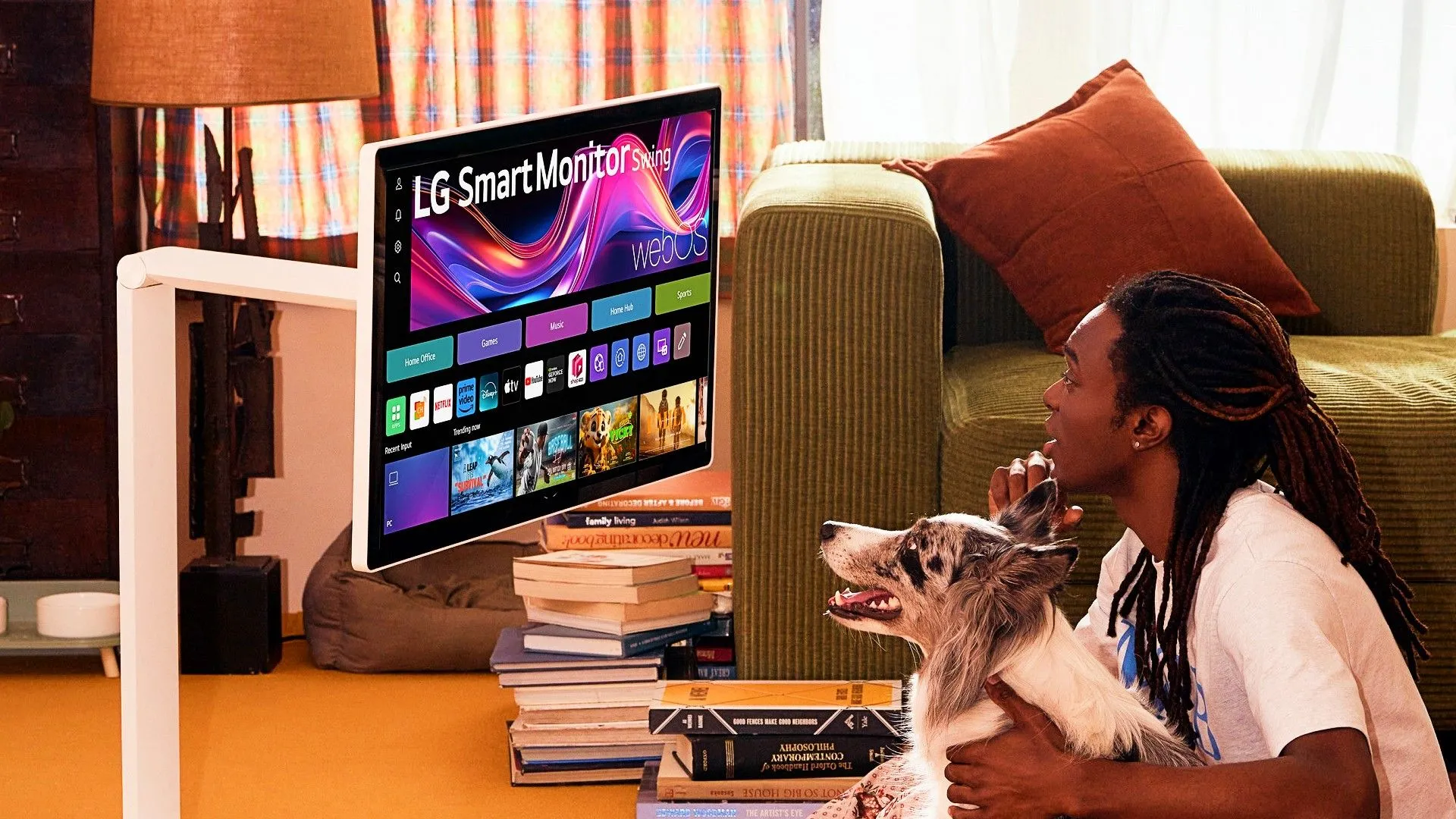 Một người đàn ông và chú chó của mình đang ngồi trên sàn nhà, sử dụng màn hình thông minh LG Smart Monitor Swing.