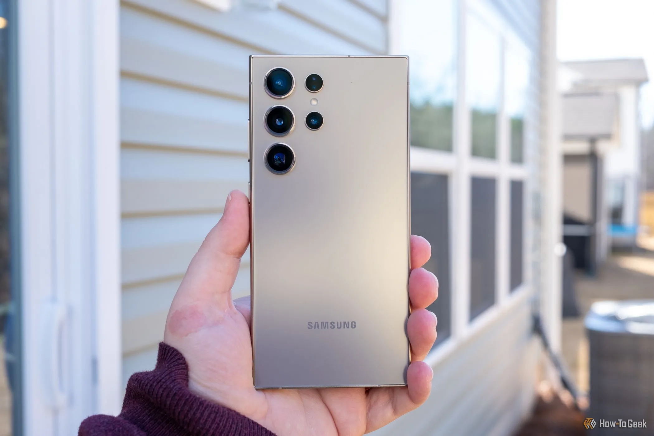 Người dùng đang cầm điện thoại Samsung Galaxy S24 Ultra màu xám, nhìn từ mặt lưng.